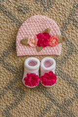 Pink baby hat and shoes with floral decorations on a textured surface