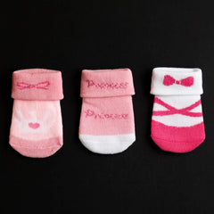 Three pairs of pink baby socks with 'Princess' and ballet design on a black background