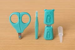 Set of teal baby care tools including scissors, toothbrush, and container on a beige background