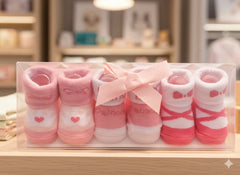 Set of pink baby socks with hearts and bows in a clear box on a wooden surface.