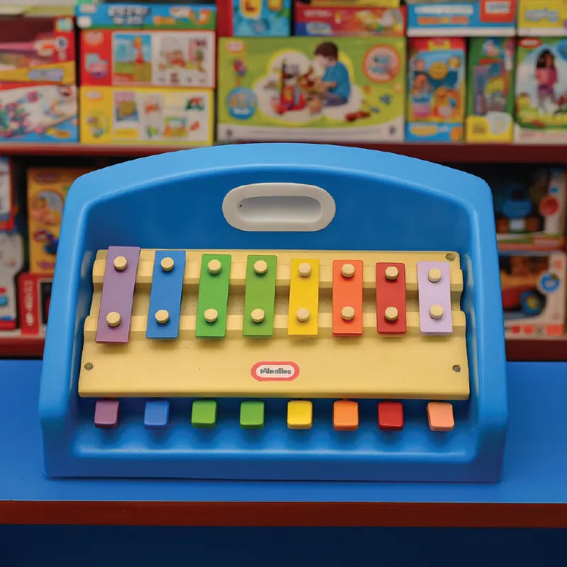 Colorful toy keyboard with a blue frame on a blue surface, surrounded by toy boxes in the background.