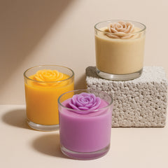 Three small glass containers with colorful rose-shaped candles on a textured surface.