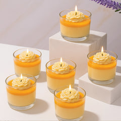 Set of six small glass jars with yellow candle melts and lit candles on a white surface.